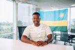 Dorcy Shema seating in an office with a Rwandan Flag behind him